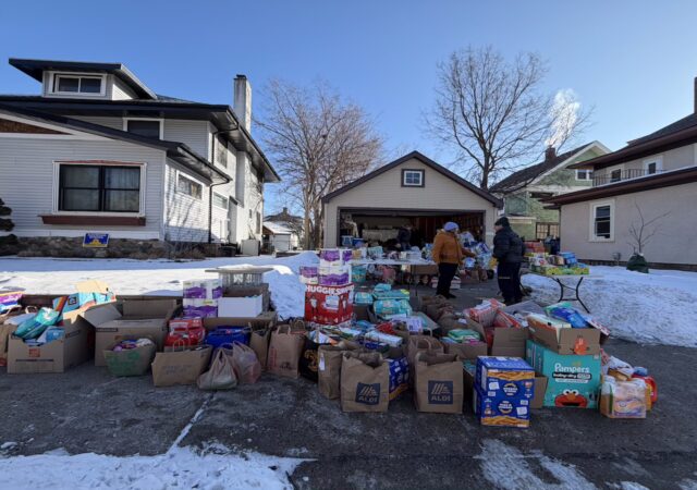 Many bags and boxes of household goods and groceries spilling out of a garage and onto the driveway and sidewalk.