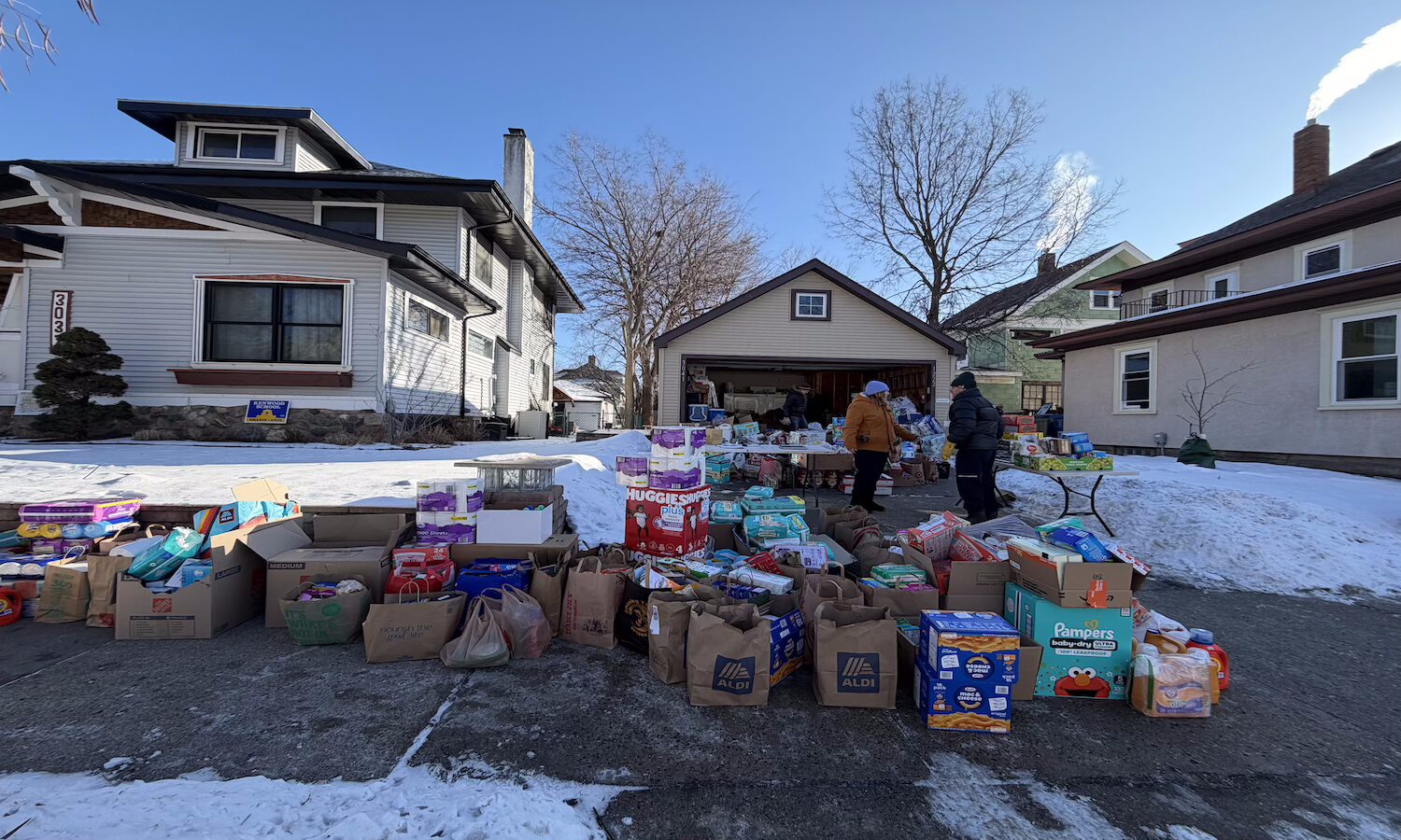 Many bags and boxes of household goods and groceries spilling out of a garage and onto the driveway and sidewalk.